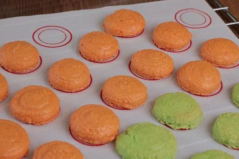 Macarons halves on baking mat on kitchen table. Orange and green cookie cutters Stock Photos