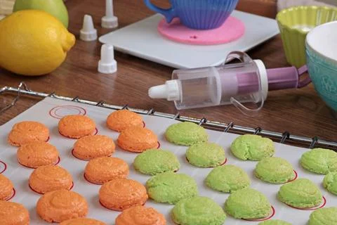 Macarons halves on baking mat on kitchen table. Orange and green cookie cutters Stock Photos