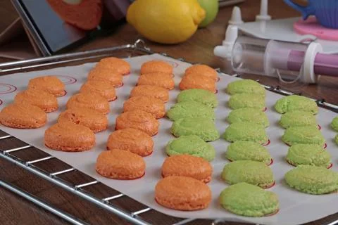 Macarons halves on baking mat on kitchen table. Orange and green cookie cutters Stock Photos