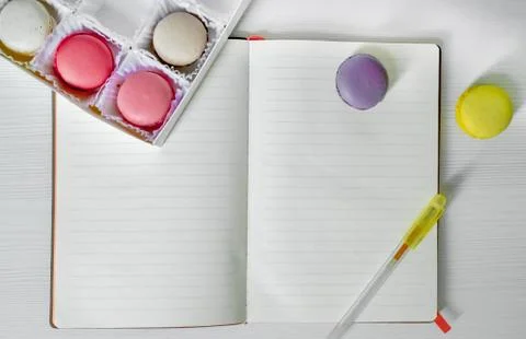 Macaroons cookies on the table next to an open notebook and pen. view from above Stock Photos