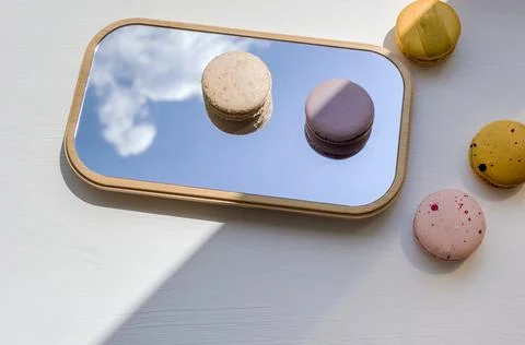 Macaroons of different colors on the mirror. A reflection of the sky and sweets Stock Photos