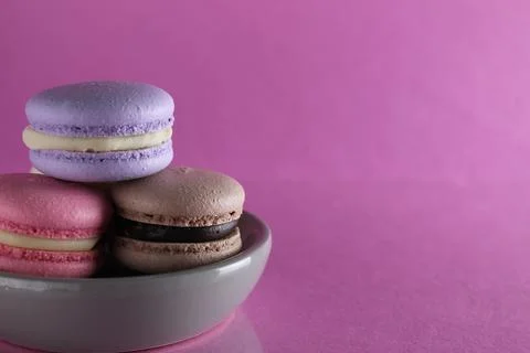 Macaroons three multicolored on a gray saucer plate stands on a pink backgrou Stock Photos
