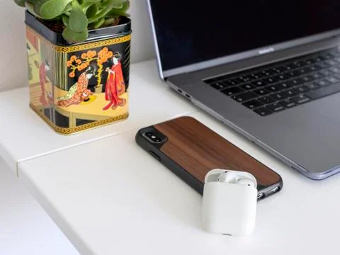 Macbook pro, airpods case, iphone in wooden cover on white table with plant Stock Photos