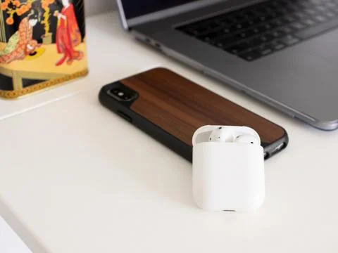 Macbook pro, airpods case, iphone in wooden cover, on white table with plant Stock Photos
