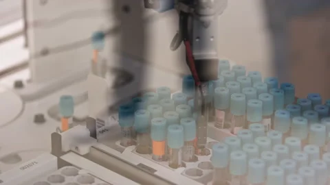 A machine hand of an automated lab taking a test tube out of a tray ad putting Stock Footage 234019113
