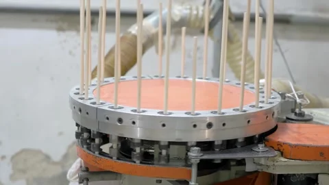A machine processes wooden dowels, arranging them vertically in a rotating .. Stockbeeldmateriaal 296483957