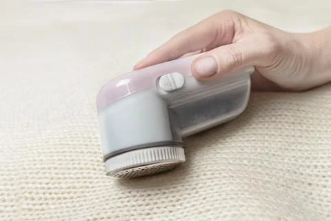 Machine for removing pellets from a woolen white jacket. A hand holds a ree.. 스톡 사진