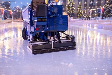 A machine for restoring or smoothing ice rides on an ice rink in the evening. Stock Photos