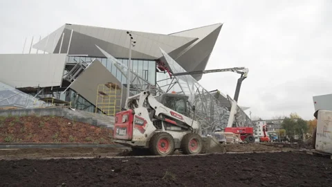 Machine shovels soil as futuristic structure gleams nearby Stock Footage 314649600