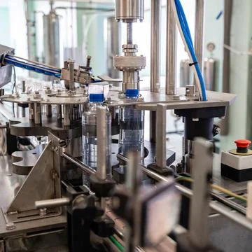 The machine tightens the lids on plastic bottles. Water production line. Stock Photos
