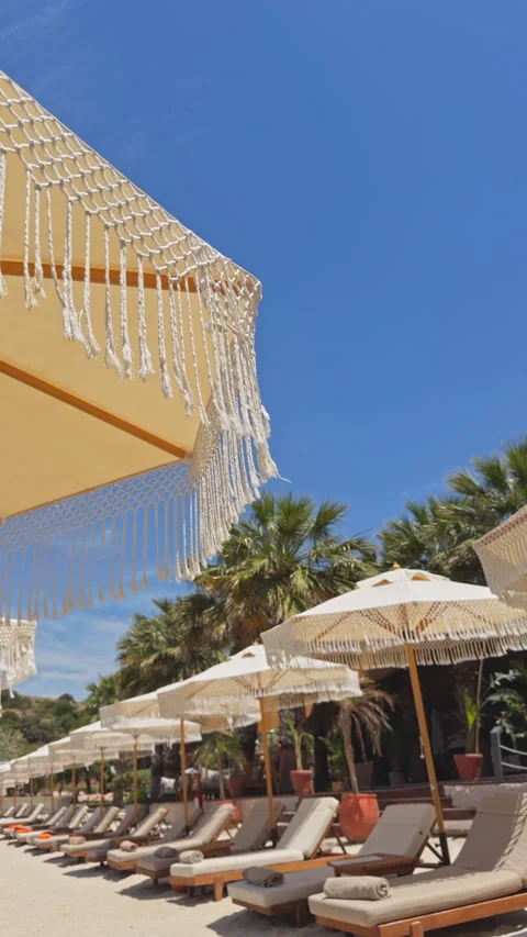 Macrame Canopy with Luxury Beach Club Sunbeds and Rocky Coast - 4K Cinematic Stock Footage 336712085