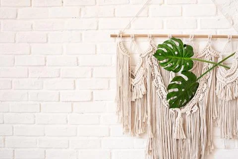 Macrame wall decor in boho style with two monstera leaves on a white brick wa Stock Photos