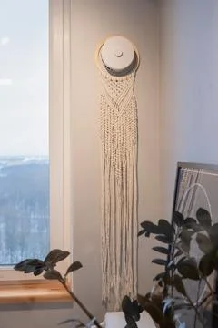 Macrame wall hanging on supply air valve on wall, window and potted plant Stock Photos