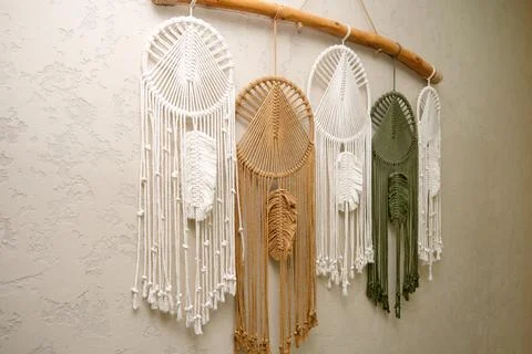 Macrame wall hanging with various feather ornaments on wooden branch. Handmad Stock Photos