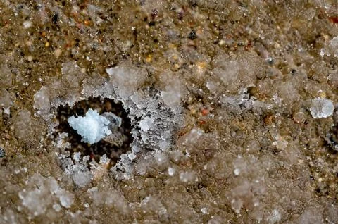 Macro above view of a single rock salt ice-melt on concrete with a frozen layer Stock Photos