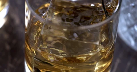 Macro of aged bourbon whiskey poured in transparent glass with ice cubes Video stock 269382263