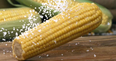 Macro of boiled yellow corn maize cob with salt is falling on wooden cut board Stock Footage 268409048