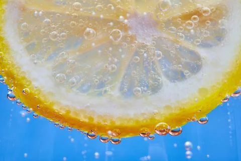 Macro of bubbles on curved edge of yellow lemon slice with blue background Stock-Fotos