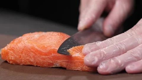 Macro. The chef's gloved hand cuts salmon meat into thin pieces with a knife. Video stock 294394486