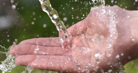 Macro of clear pure water flow stream pouring to young hand with splashing drops Stock Footage 268442032