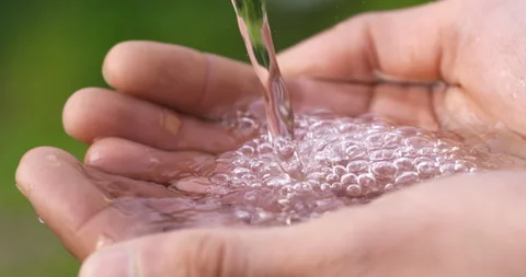 Macro of clear pure water flow stream pouring to young hand with splashing drops Stock Footage 268442153