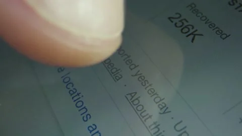 Macro close-up of finger scrolling over Corona virus articles on phone 動画素材 130596556