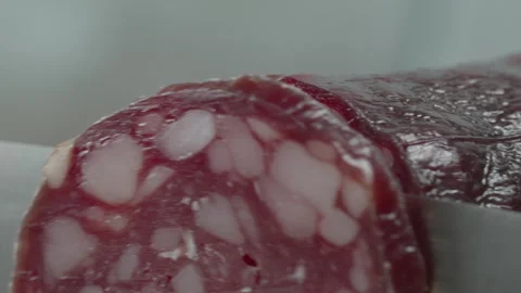 Macro close-up of a knife blade cutting a piece of smoked salami sausage 스톡 동영상 316180390