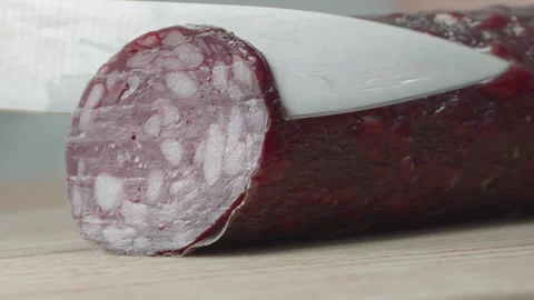 Macro close-up of a knife blade cutting a piece of smoked salami sausage 스톡 동영상 316180393