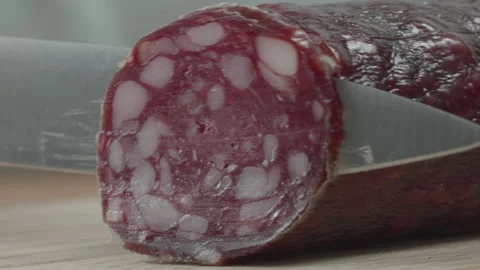 Macro close-up of a knife blade cutting a piece of smoked salami sausage 스톡 동영상 316180405