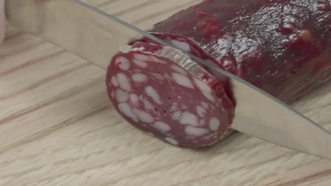 Macro close-up of a knife blade cutting a piece of smoked salami sausage 스톡 동영상 316180438