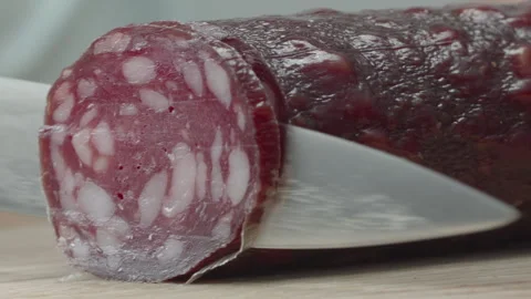 Macro close-up of a knife blade cutting a piece of smoked salami sausage 스톡 동영상 316180513