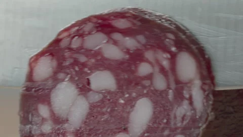 Macro close-up of a knife blade cutting a piece of smoked salami sausage 스톡 동영상 316180520