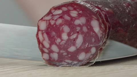 Macro close-up of a knife blade cutting a piece of smoked salami sausage 스톡 동영상 316180543