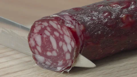 Macro close-up of a knife blade cutting a piece of smoked salami sausage 스톡 동영상 316180547