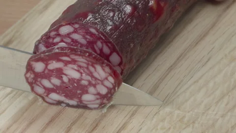 Macro close-up of a knife blade cutting a piece of smoked salami sausage 스톡 동영상 316180554