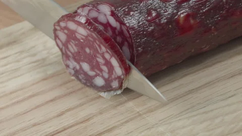 Macro close-up of a knife blade cutting a piece of smoked salami sausage 스톡 동영상 316180585