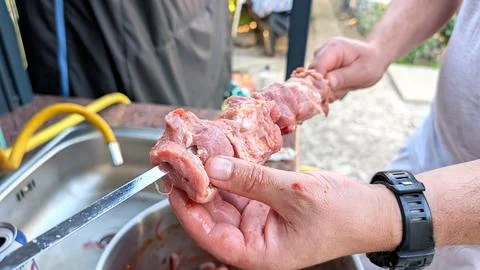 Macro close-up of man hands threading raw marinated meat onto a metal skewer  Photos