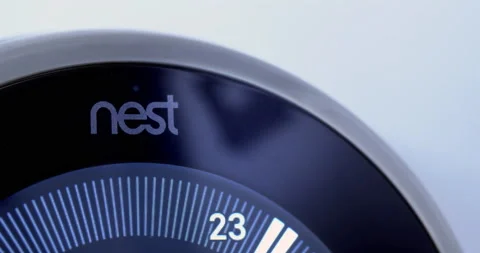 A macro close up to the Nest logo of a Nest Learning Thermostat on a white wall. Stockbeeldmateriaal 138314026