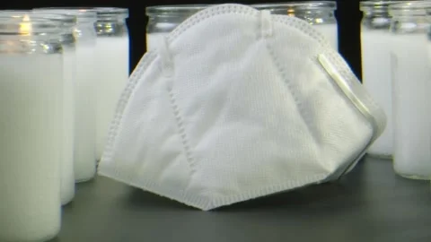 Macro close-up of a protective face mask next to white burning candles Stock Footage 132212067