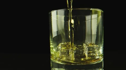 Macro close-up shot of alcohol being poured on a glass. Background is black. Stock Footage 131753391