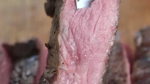 Macro Close-up of Slicing a Juicy Grilled Medium-Rare Ribeye Steak on a Wooden B Stock Footage 338210754