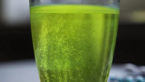 Macro close up of a soluble effervescent tablet dissolving in a glass of greenis Stock Footage 341827416