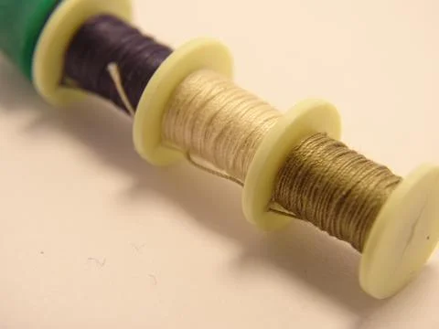 Macro close‑up of three thread spools in coordinated colors on a light surface Foto stock