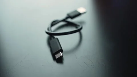 Macro close-up of a USB-C charging cable on a dark desk with shallow depth of Vídeos de archivo 328974644