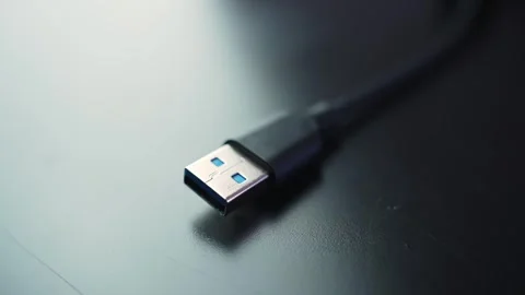 Macro close-up of a USB-A plug on a black cable resting on a dark desk with Stock Footage 329479949