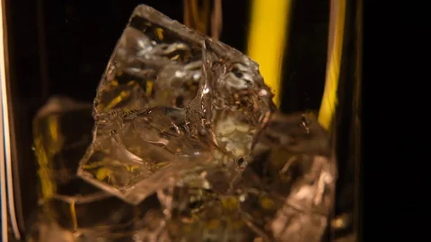 Macro close up of  Whiskey being poured onto Ice cubes in glass of whisky Stock Footage 128574578