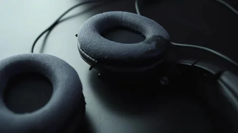 Macro close-up of worn over-ear headphone ear pad with cable on dark desk Stock Footage 329480415