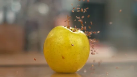 MACRO, DOF: Tiny brown flax seeds fall from the air and onto the yellow apple. Stock Footage 103185539