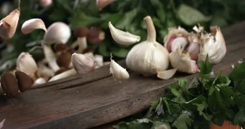 Macro of falling fresh garlic cloves on bulbs and parsley on wooden cut board Stock Footage 268983345