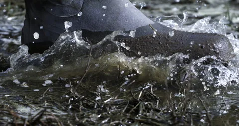 Macro of farmer in rubber boots walks through mud puddles with splashing water Stock-Footage 268230223